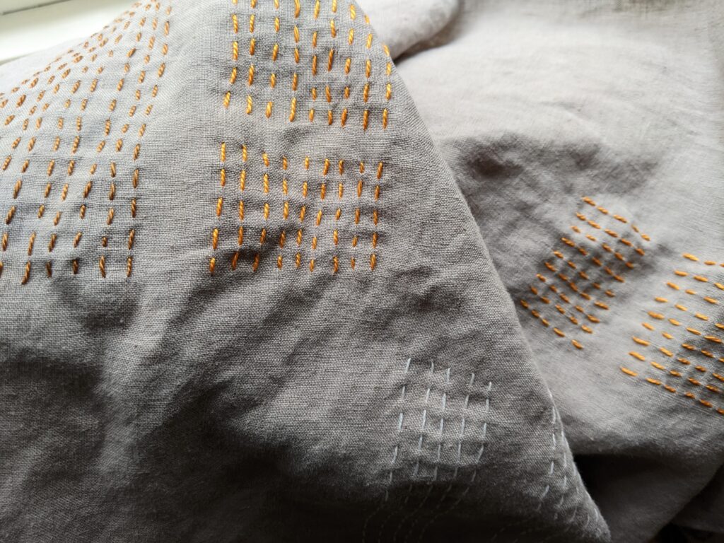 Natural linen towels are made from repurposed clothing with rust-colored sashiko stitches applied in parallel rows to create geometric shapes 